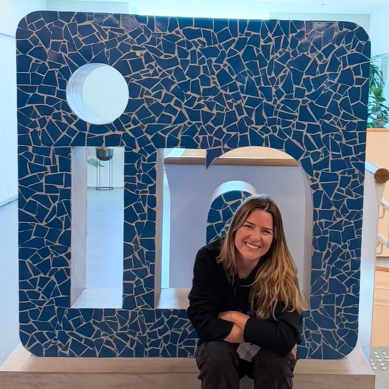 Andreza Araújo sentada em um letreiro gigante do LinkedIn